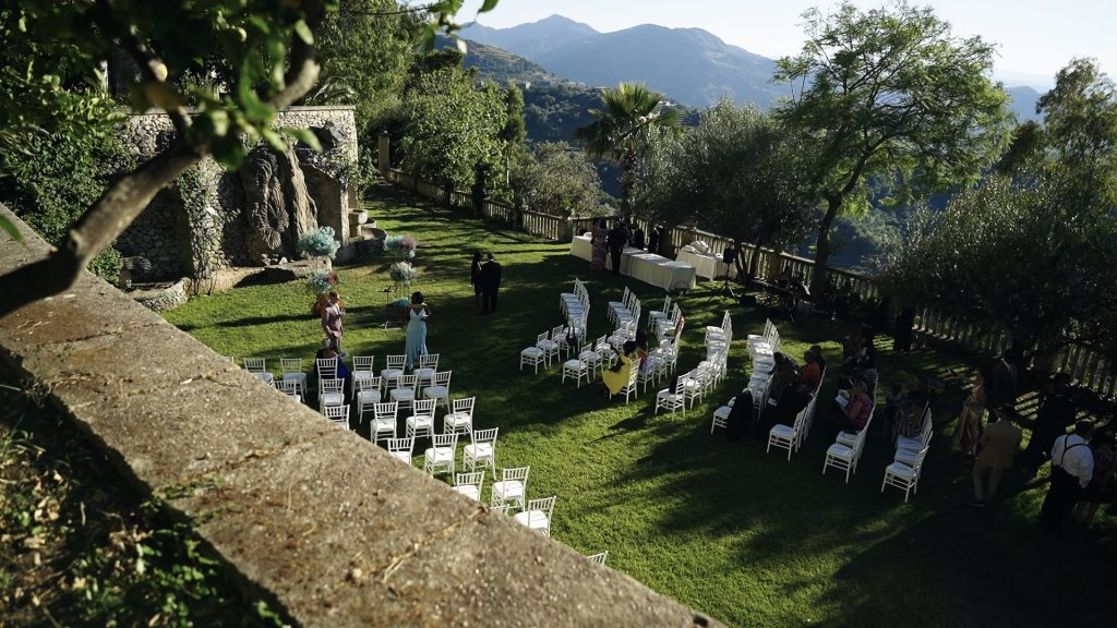 view of the garden with green grass of a Sicilian wedding venue surrounded by trees and with white seats in a semicercle set up for the destination wedding of Federico and Anissa