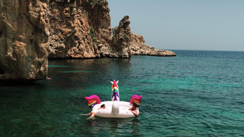 the newlyweds during their beach party on a unicorn-shaped dinghy among the spectacular rocky cliffs the day after their destination wedding