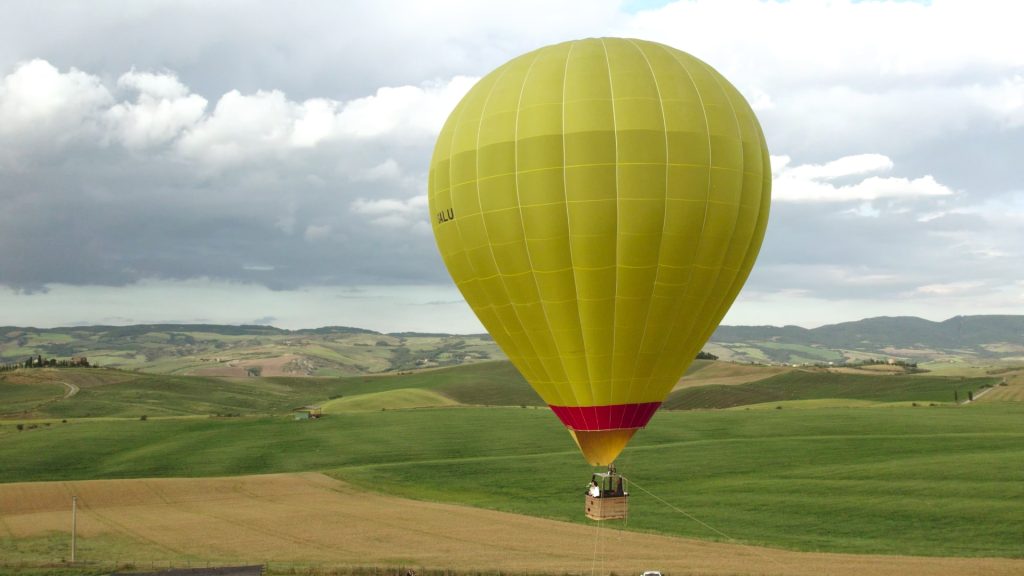 hot air balloon with the newlyweds among the green Tuscan hills in Val d'Orcia during their destination wedding