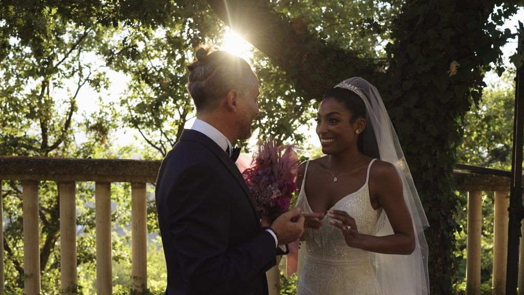 the newlyweds look at each other smiling after having just gotten married surrounded by trees at sunset