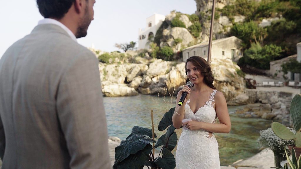 the bride and groom during their vows on the seashore next to the rocks overlooking the sea