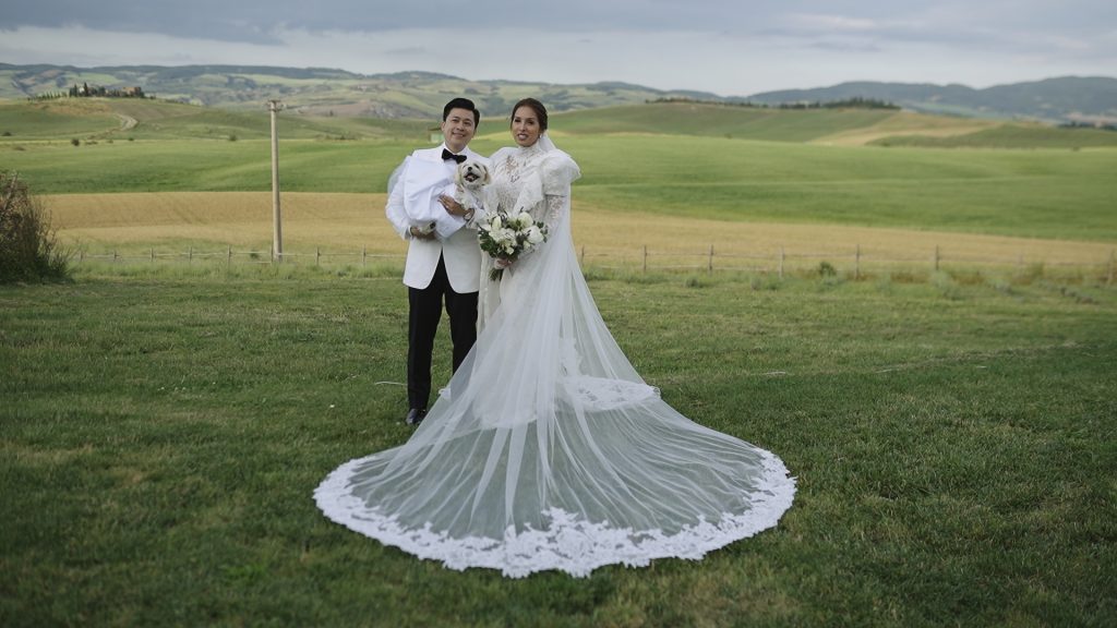 the bride and the groom take a photo together with their dog with the green Tuscan hills in the background