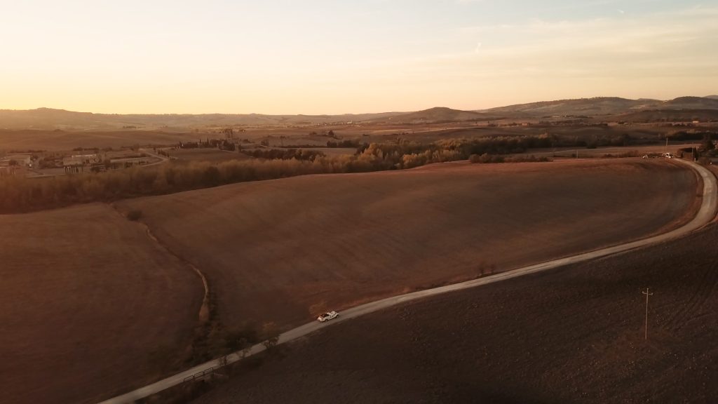 Road with car between tuscan hills at the sunset light